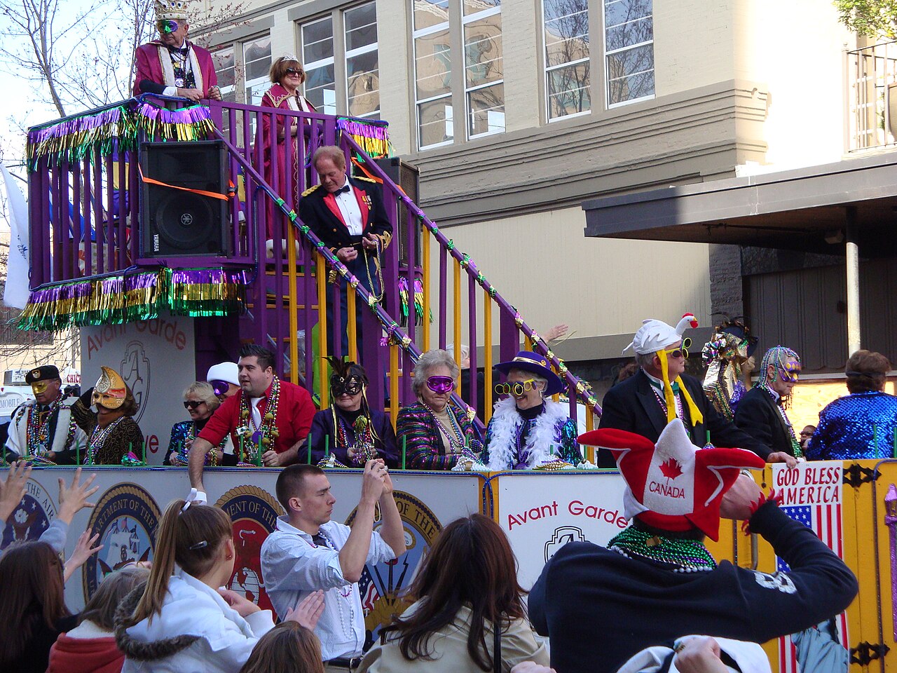 A Mardi Gras krewe float and cheering crowd on a downtown Pensacola street, decorated in purple and gold